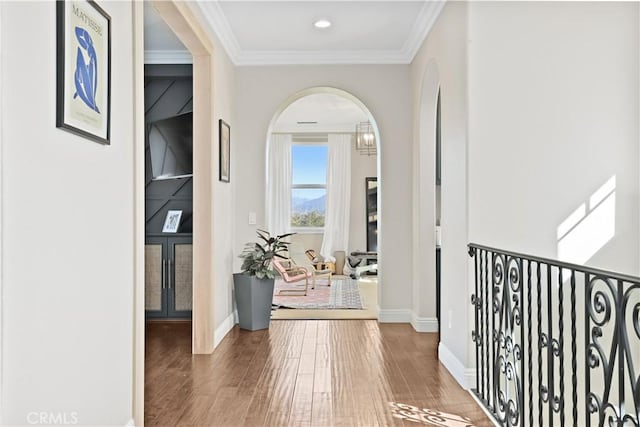 hall featuring arched walkways, crown molding, baseboards, and wood finished floors