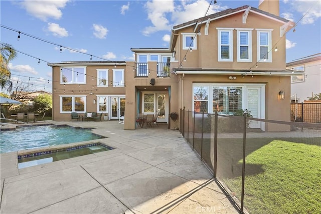 rear view of house featuring a balcony, an in ground hot tub, a fenced backyard, stucco siding, and a patio area