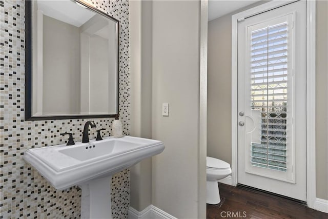 bathroom with toilet, a sink, wood finished floors, decorative backsplash, and baseboards