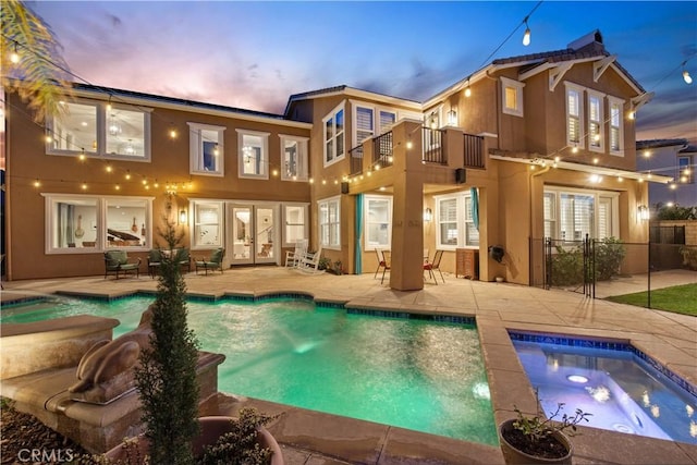 rear view of house with french doors, a balcony, a hot tub, and a patio area