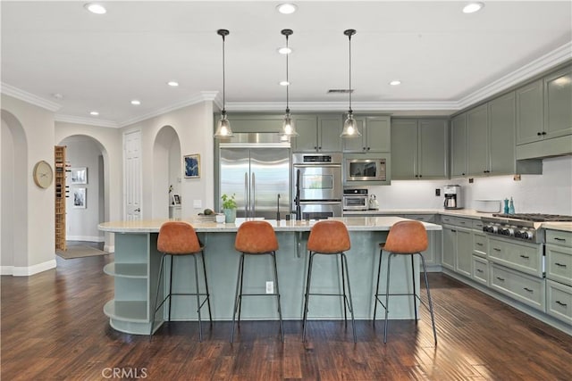 kitchen with dark wood-style floors, built in appliances, a breakfast bar area, and ornamental molding