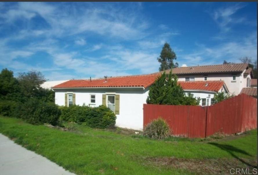 view of property exterior with a yard, a tile roof, fence, and stucco siding