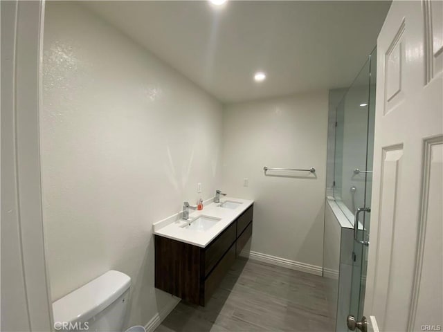 bathroom featuring a shower with shower door, toilet, baseboards, and a sink