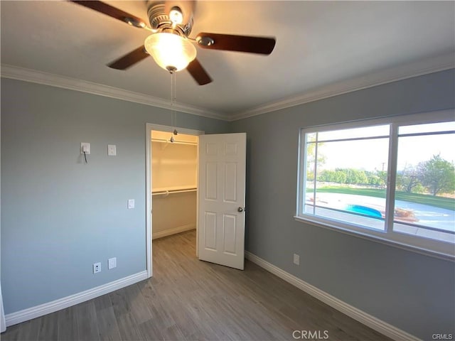 unfurnished bedroom featuring a walk in closet, wood finished floors, baseboards, and ornamental molding