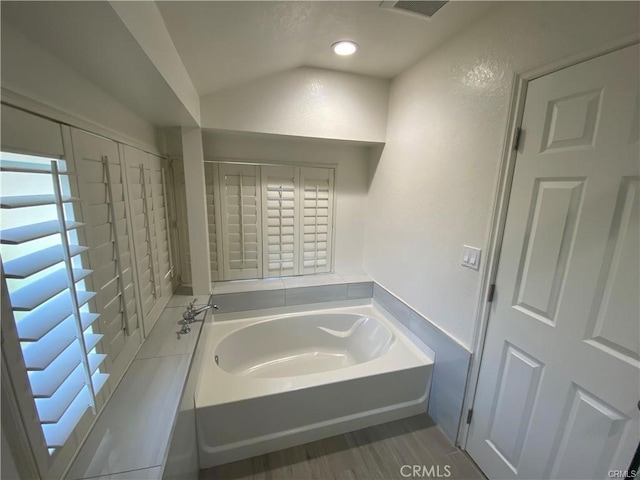 full bath featuring visible vents, lofted ceiling, a bath, and a textured wall