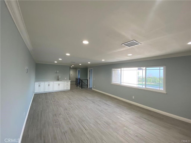 empty room with visible vents, baseboards, light wood-style flooring, and crown molding