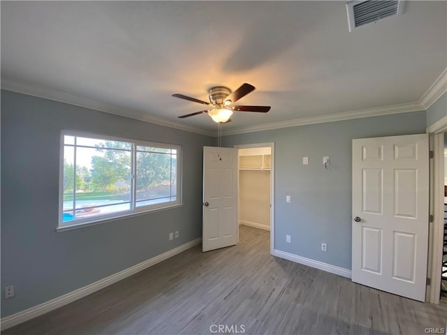 unfurnished bedroom with visible vents, crown molding, wood finished floors, and baseboards