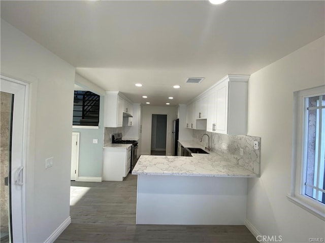 kitchen with visible vents, a peninsula, freestanding refrigerator, a sink, and gas range oven