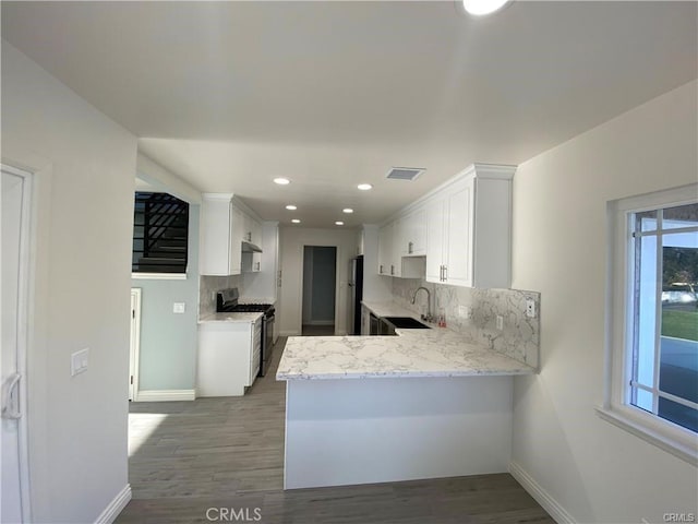 kitchen with stainless steel range with gas cooktop, a peninsula, a sink, decorative backsplash, and white cabinets