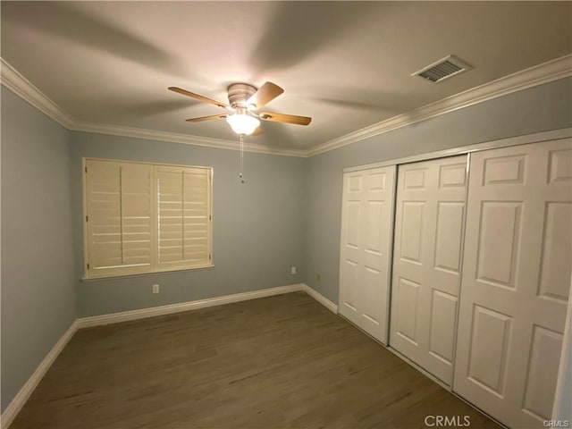 unfurnished bedroom featuring visible vents, crown molding, dark wood-type flooring, baseboards, and a closet