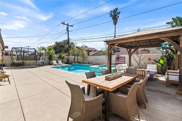 view of swimming pool with outdoor dining space, a pool with connected hot tub, a trampoline, a fenced backyard, and a patio area