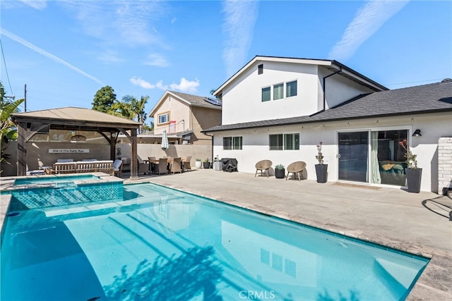 rear view of property featuring a gazebo, stucco siding, a pool with connected hot tub, and fence