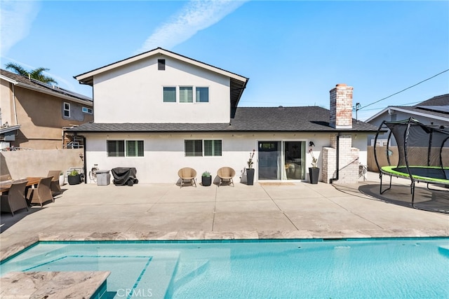 back of property with a patio, fence, a chimney, stucco siding, and a trampoline