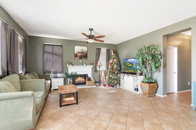 living room featuring ceiling fan, light tile patterned flooring, baseboards, and a glass covered fireplace