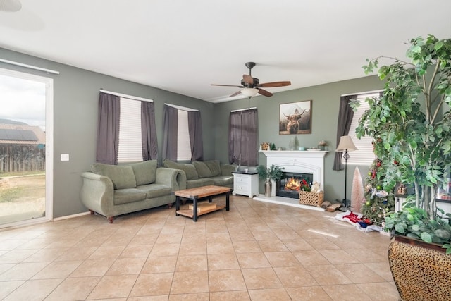 living area featuring a glass covered fireplace, light tile patterned flooring, plenty of natural light, and ceiling fan