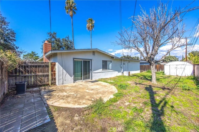 rear view of property with an outbuilding, a patio, stucco siding, a storage unit, and a fenced backyard