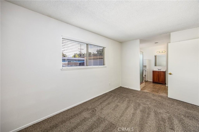 unfurnished bedroom featuring carpet, ensuite bath, a textured ceiling, and baseboards