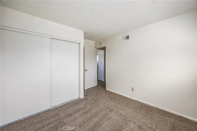 unfurnished bedroom featuring a closet, visible vents, carpet flooring, a textured ceiling, and baseboards