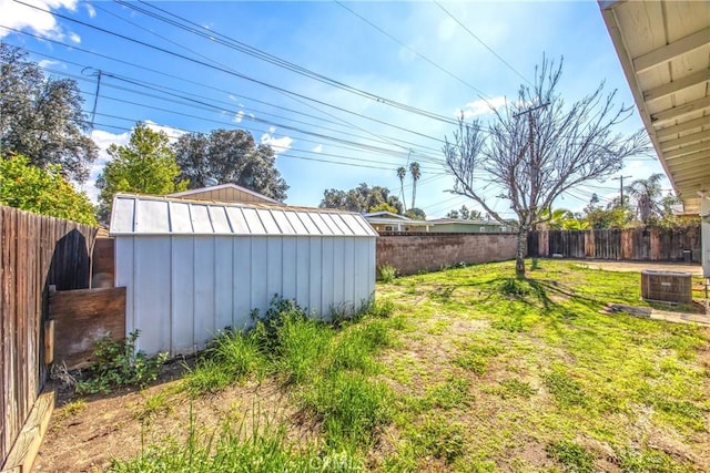 view of yard with a shed, a fenced backyard, central AC unit, and an outdoor structure