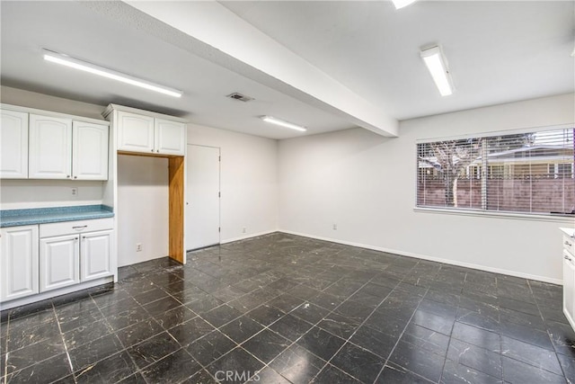 empty room with beam ceiling, visible vents, and baseboards