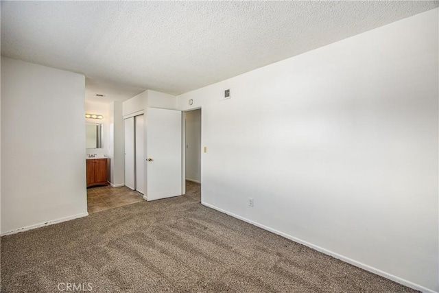 unfurnished bedroom with carpet floors, connected bathroom, a textured ceiling, and baseboards