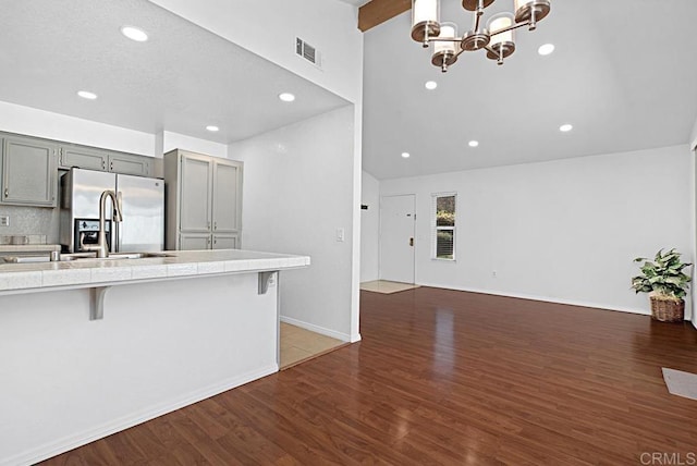 kitchen with a breakfast bar area, gray cabinetry, dark wood-style flooring, visible vents, and stainless steel refrigerator with ice dispenser