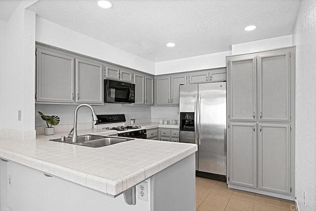 kitchen featuring black microwave, gray cabinetry, a sink, stainless steel fridge with ice dispenser, and gas stove