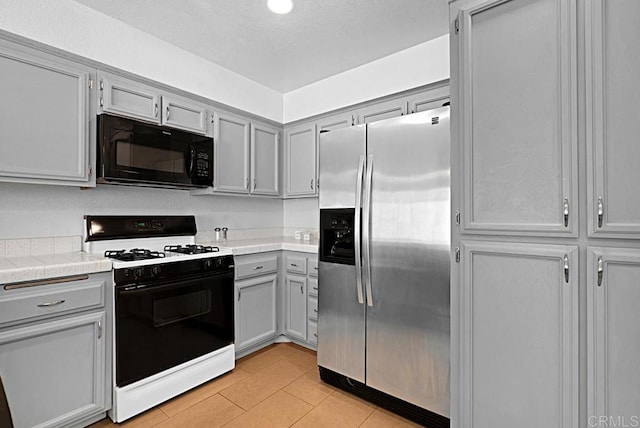 kitchen featuring black microwave, gray cabinetry, light countertops, stainless steel fridge, and gas range