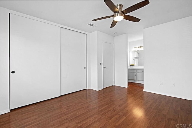 unfurnished bedroom with a closet, visible vents, ensuite bathroom, dark wood-type flooring, and ceiling fan