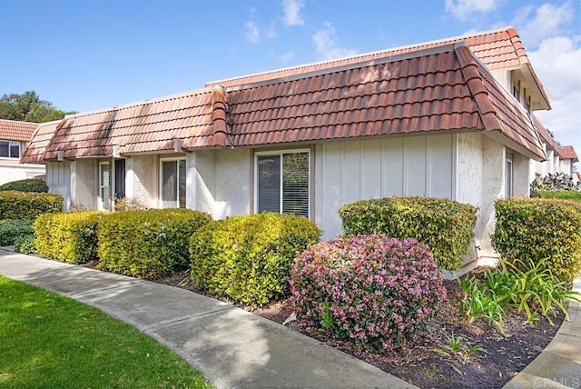 view of side of property featuring stucco siding, a tiled roof, and mansard roof