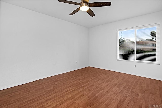 spare room with wood finished floors, a ceiling fan, and baseboards