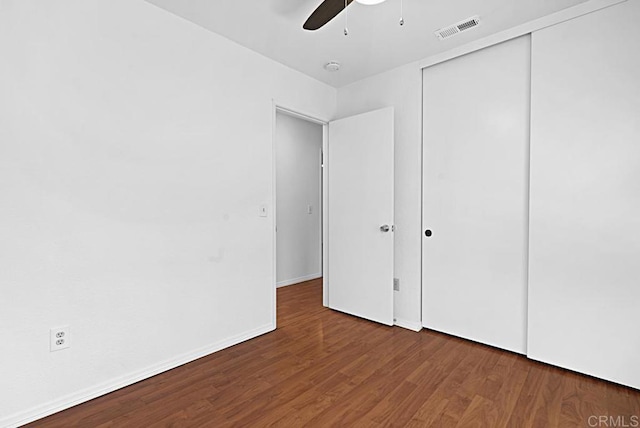 unfurnished bedroom with baseboards, visible vents, ceiling fan, wood finished floors, and a closet