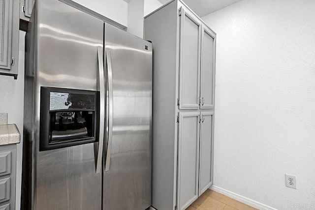 kitchen featuring light tile patterned floors, stainless steel fridge with ice dispenser, light countertops, gray cabinetry, and baseboards