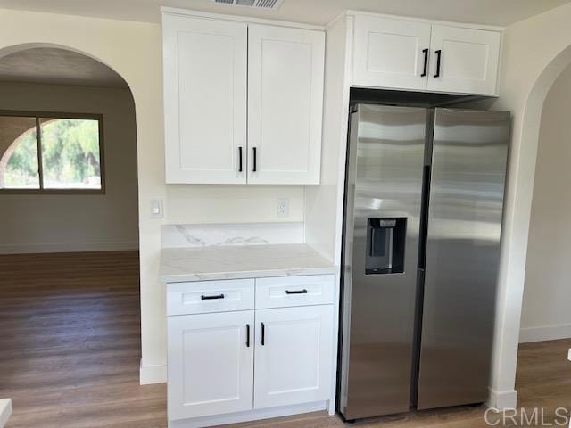 kitchen featuring light stone counters, stainless steel refrigerator with ice dispenser, light wood-style flooring, white cabinetry, and baseboards