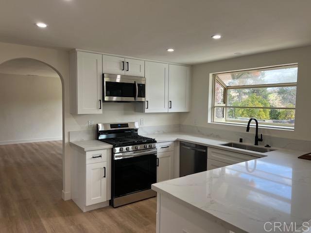 kitchen featuring arched walkways, white cabinets, appliances with stainless steel finishes, light wood-type flooring, and a sink