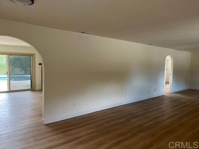 spare room with arched walkways, dark wood-type flooring, visible vents, and baseboards