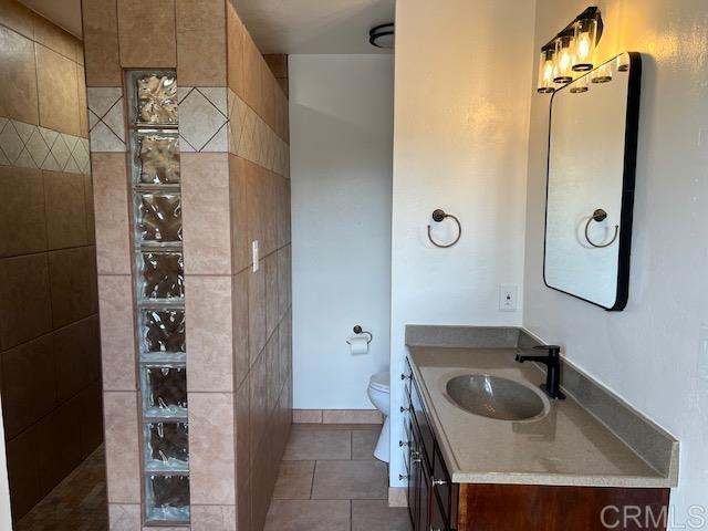 full bathroom featuring toilet, tile patterned floors, a walk in shower, and vanity