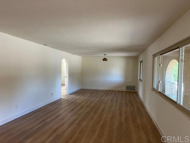 empty room featuring arched walkways, visible vents, baseboards, and wood finished floors