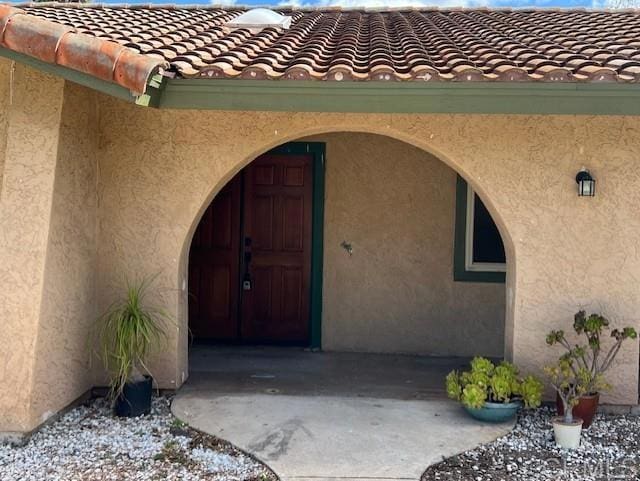 doorway to property featuring a tile roof and stucco siding