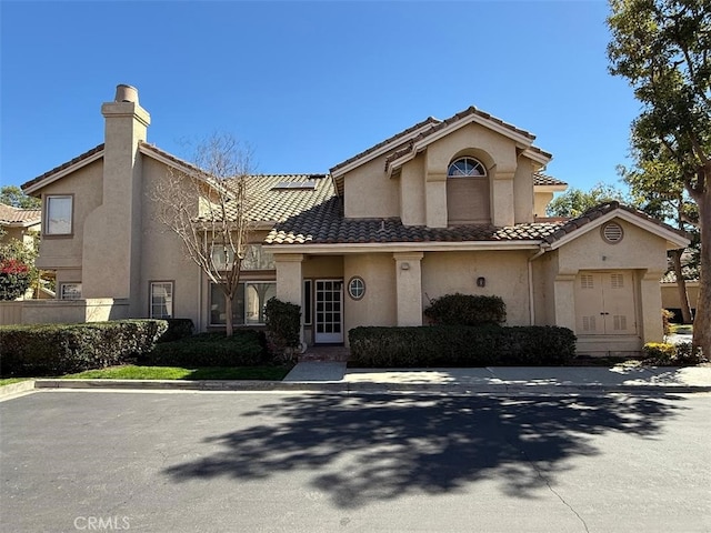 view of front of property featuring a tile roof, a chimney, and stucco siding