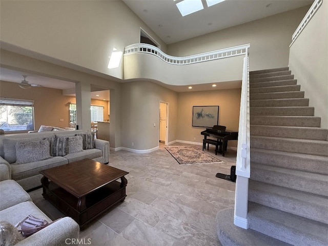 living area with a skylight, baseboards, stairway, and a high ceiling