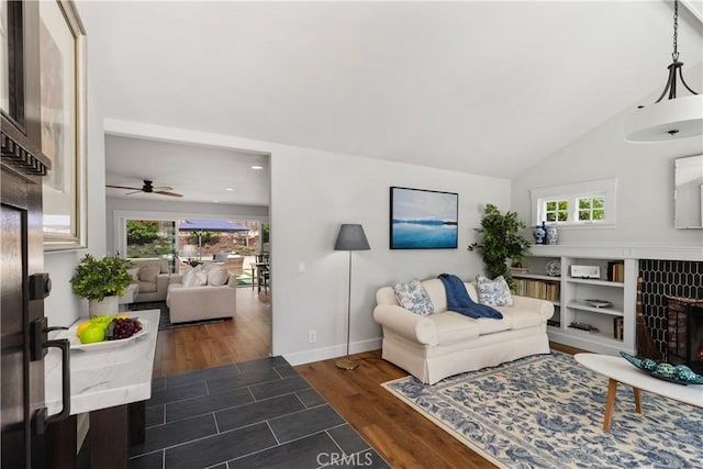 living room with ceiling fan, baseboards, lofted ceiling, a warm lit fireplace, and wood finished floors