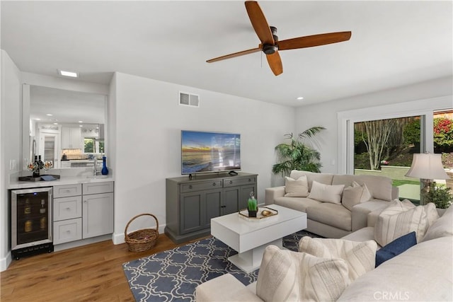 living room with wine cooler, visible vents, baseboards, and wood finished floors