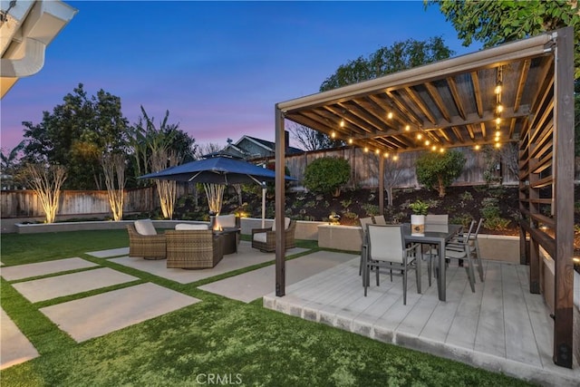 patio terrace at dusk featuring an outdoor living space, outdoor dining area, a lawn, and a fenced backyard