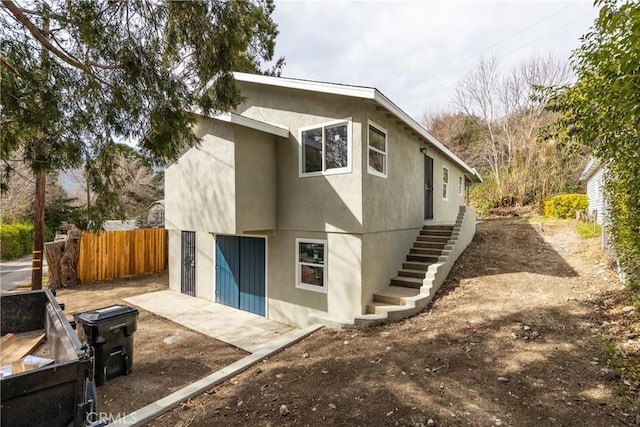 rear view of property featuring stairs, fence, and stucco siding