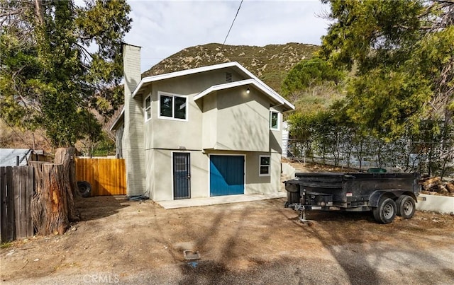 back of house featuring a chimney, fence, and stucco siding