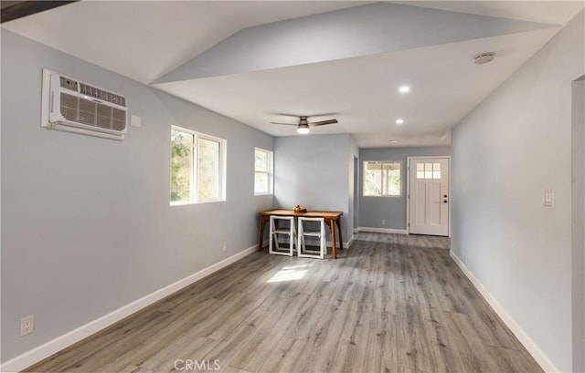 foyer featuring light wood finished floors, an AC wall unit, vaulted ceiling, ceiling fan, and baseboards