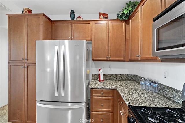 kitchen with brown cabinetry, stone counters, and appliances with stainless steel finishes