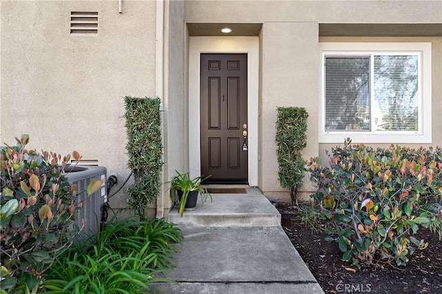 entrance to property featuring stucco siding and cooling unit