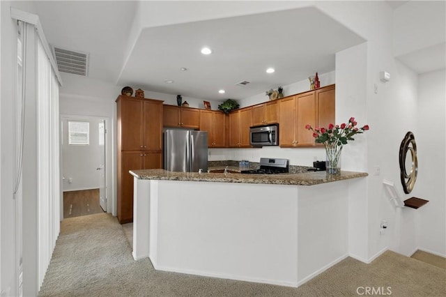 kitchen featuring visible vents, light colored carpet, dark stone counters, brown cabinets, and appliances with stainless steel finishes